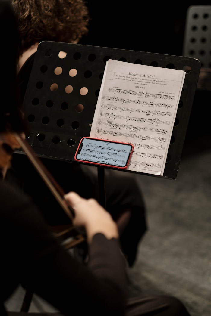Musician playing a bowed string instrument while reading sheet music during a concert.